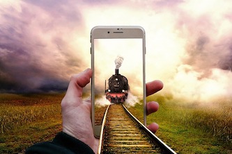 Train in a phone held by a hand matching the scenery. optical illusion
